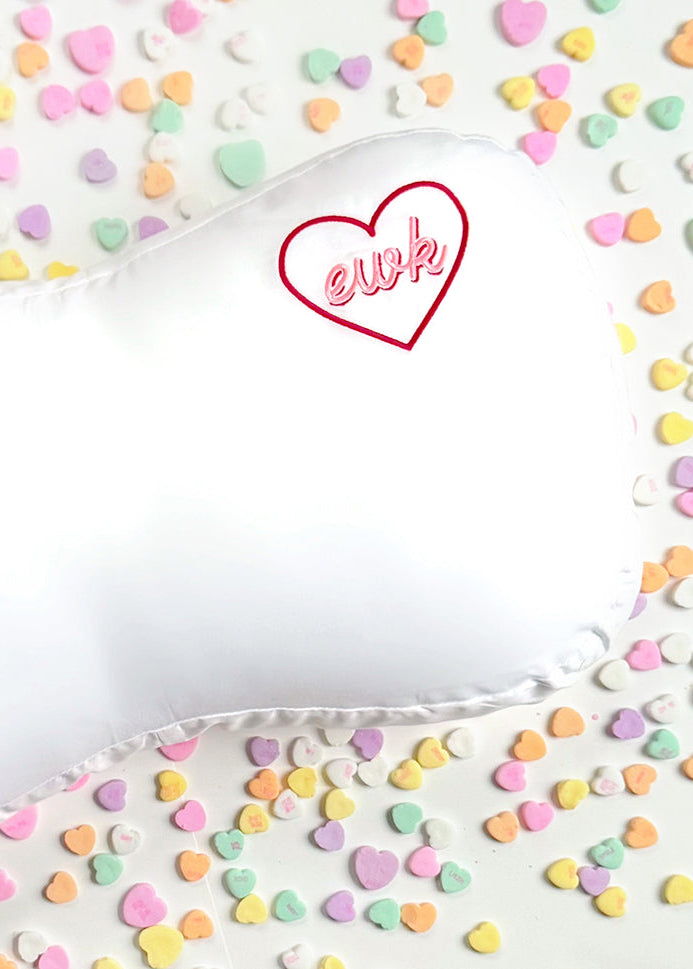 Heart-shaped pillow with 'ewk' text on a background of colorful heart-shaped candies